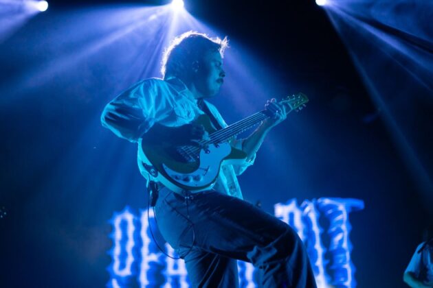 A person performs on stage with a guitar under a spotlight