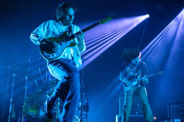 A band performs on a stage under purple lighting.