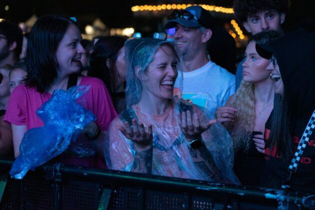 A person smiles, in a rain poncho, in a crowd of people at a concert.