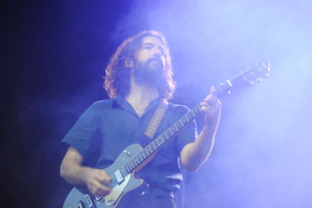 A man with an electric guitar on a stage with purple lighting plays.
