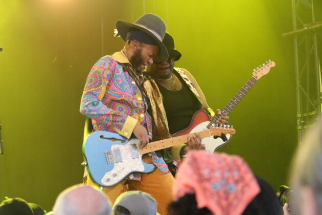 Two people with guitars perform side-by-side on stage.