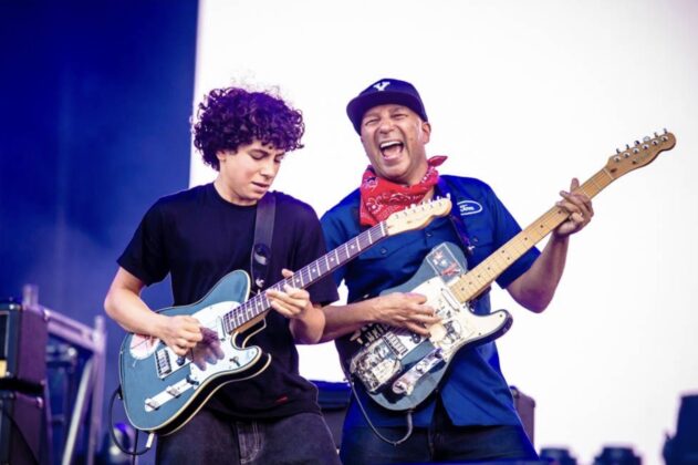 A father and son play guitar on a stage.