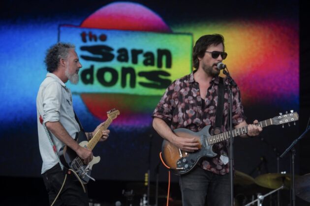 A band performs in front of a rainbow background.