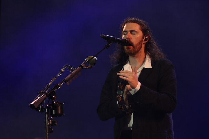 A man passionately sings on a blue-lit stage at night. 