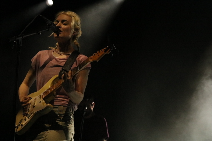 A person with a guitar sings on a dark stage