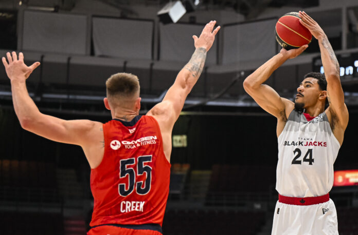 BlackJacks player holds basketball over head to shoot over opponent.