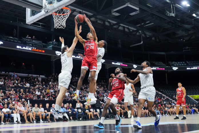 Basketball player wearing red reaches to the basket surrounded by players wearing white.