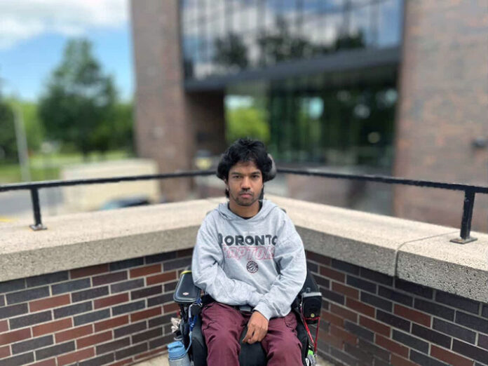 maheeshanportrait_720 A person in a wheelchair wearing a gray sweater stares into the camera.