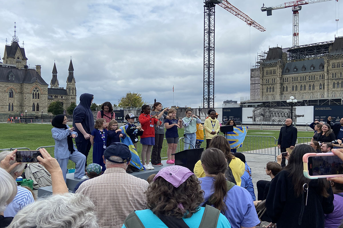 A group of children stand on stage on Parliament Hill and are signing with their hands.