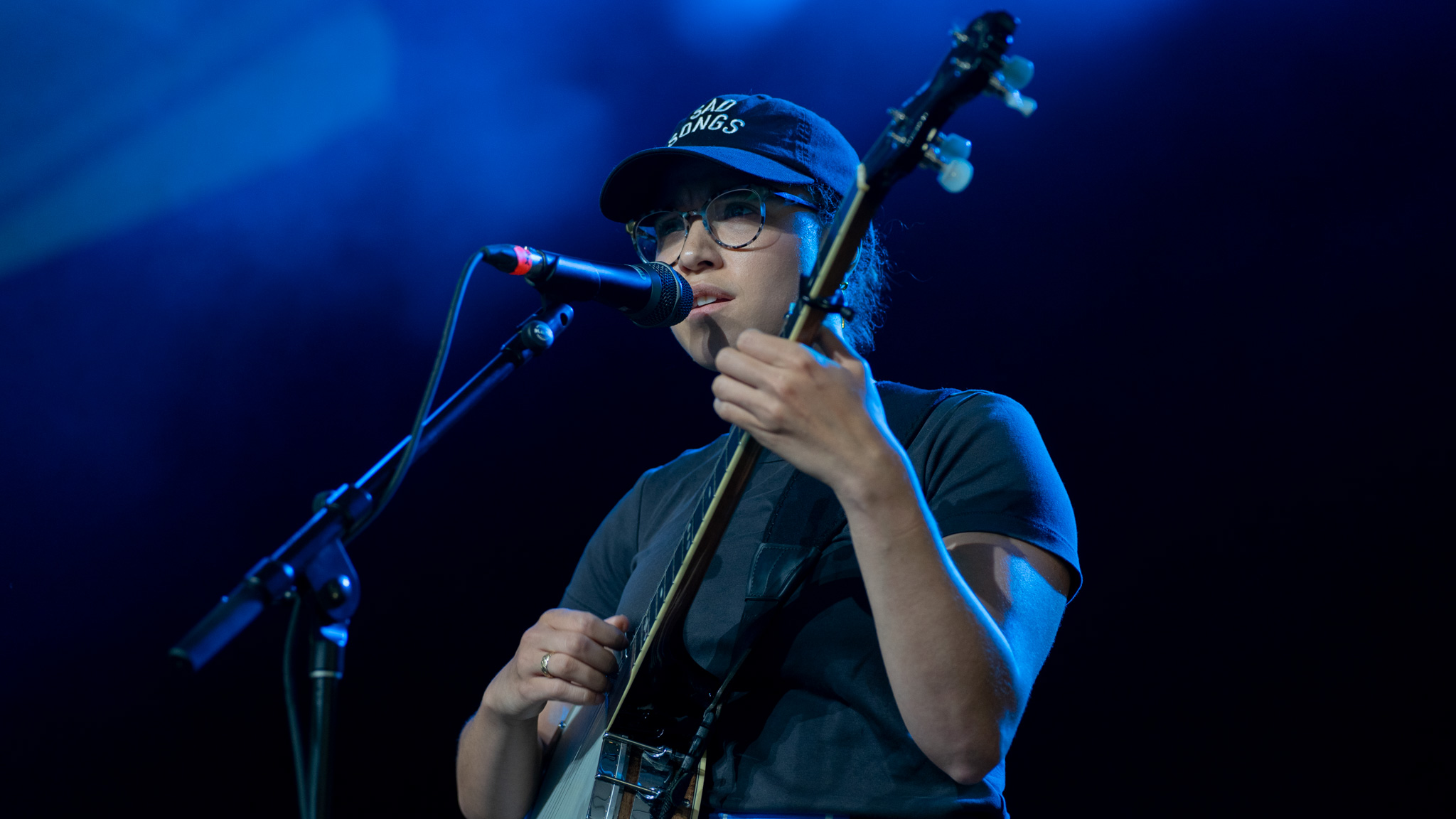 A singer performs on stage in dark clothing under a blue spotlight.