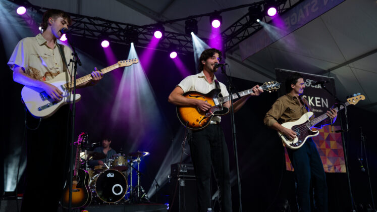 A three-piece performs under purple lighting on stage.