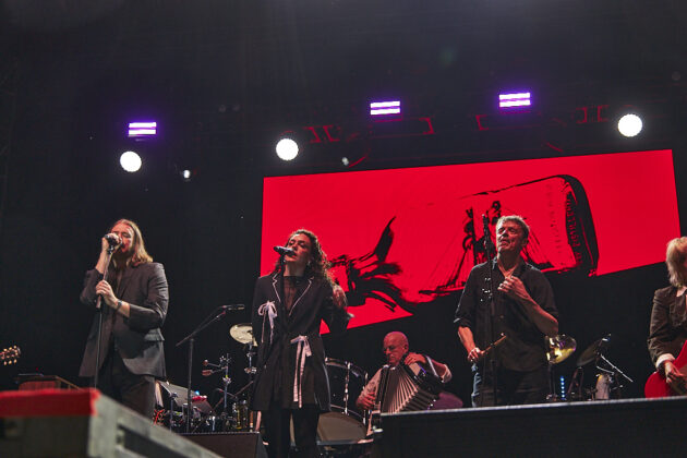 A band performs on stage in front of a red background.