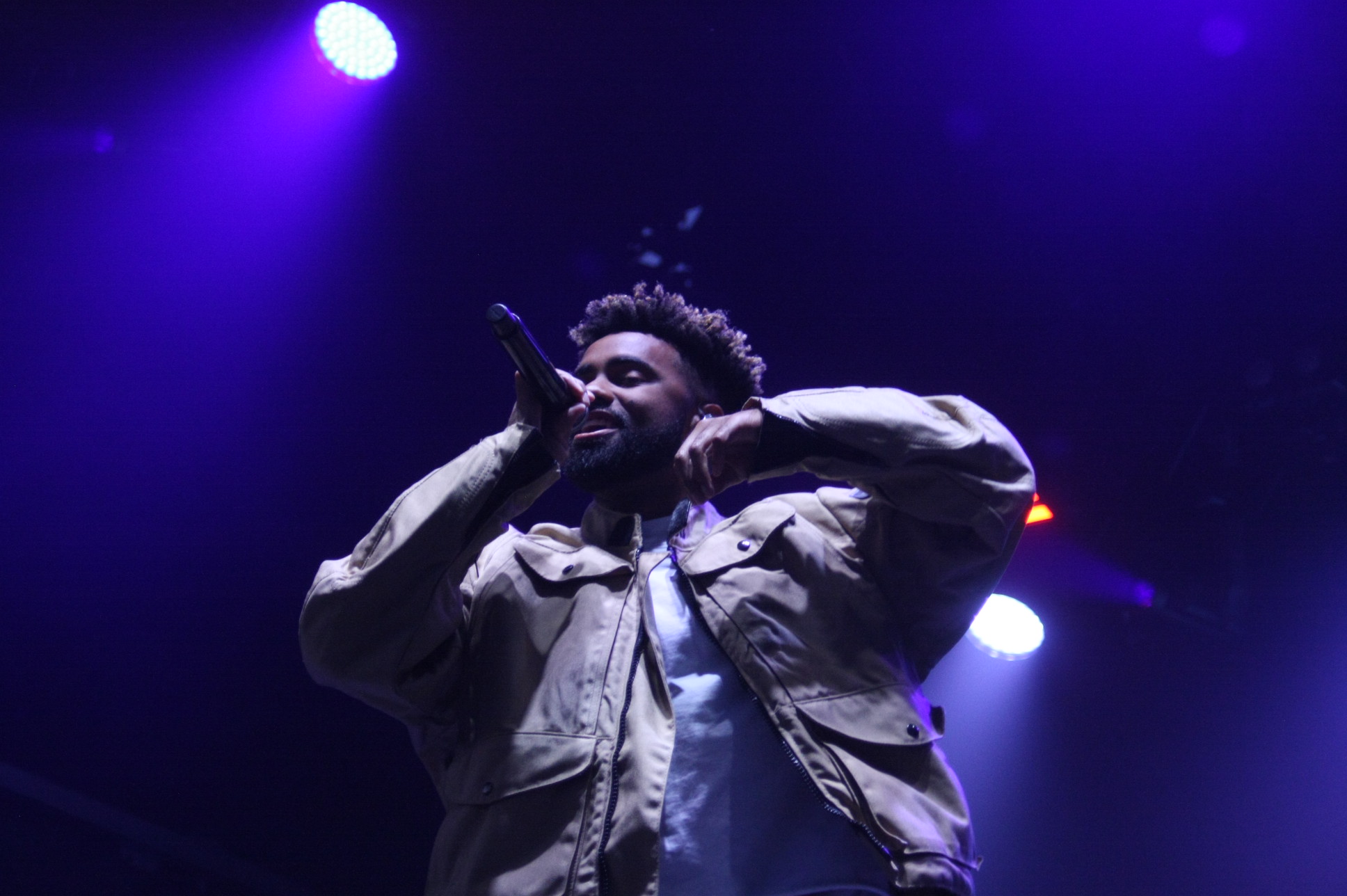 A singer smiles and dances on stage under purple-blue lighting at night.