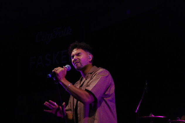 A singer closes his eyes and sings passionately at night on stage.
