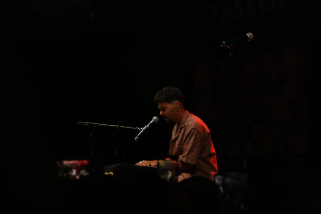 A singer performs at the piano and sings on stage at night.