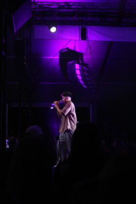 A singer sings on stage at night under purple lighting.