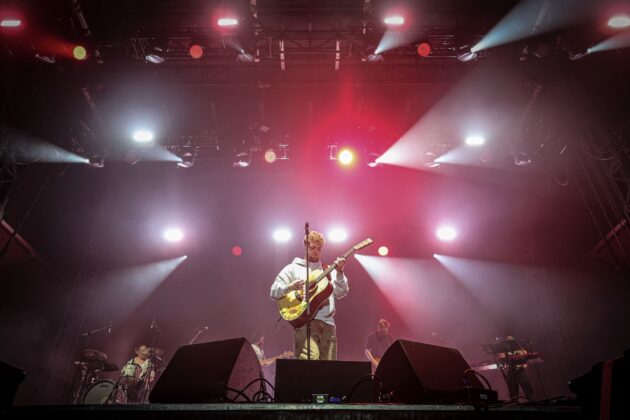 A singer performs on stage against red and white spotlights at night.