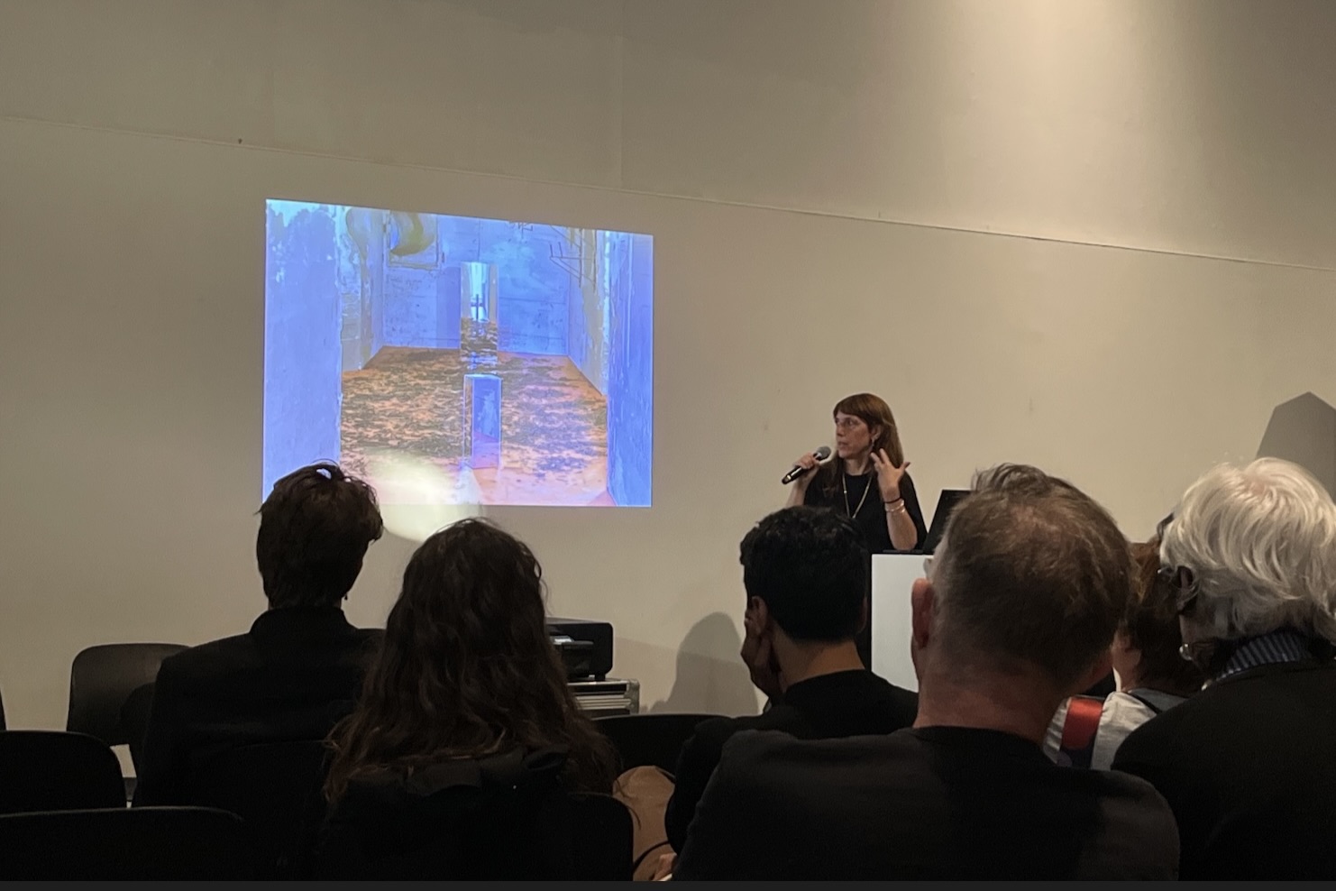 An artist explains her work projected onto the wall in front of a crowd.