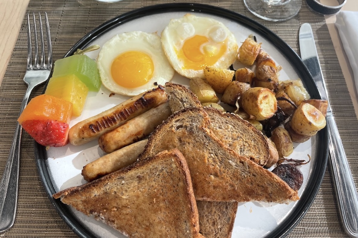 A breakfast plate with toast, two eggs, homefries and fruit sits on a table.