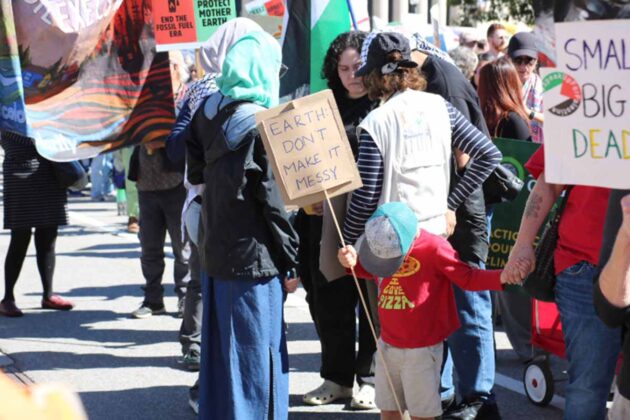 child holds sign saying 'earth don't make it messy' in a crowd of people