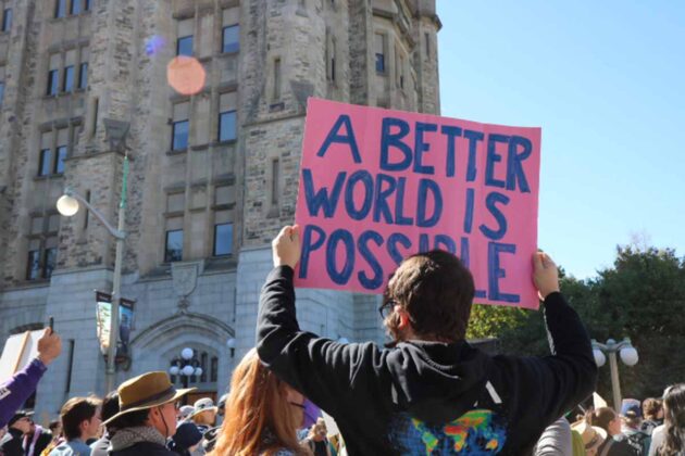 a person in a crowd holds a sign reading 'a better world is possible'
