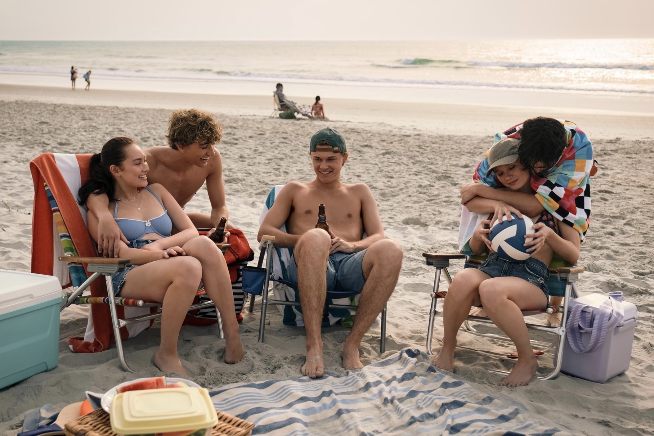 A group of five people are smiling and sitting at the beach.