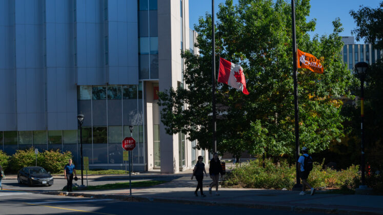 An every child matters flag and a canada flag are at half mast on flagpoles by Richcraft Hall building