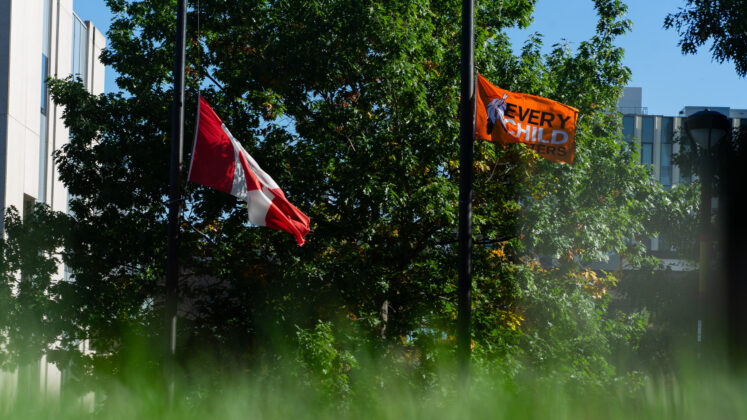 Canada flag and Every Child Matters flag are at half mast on the pole