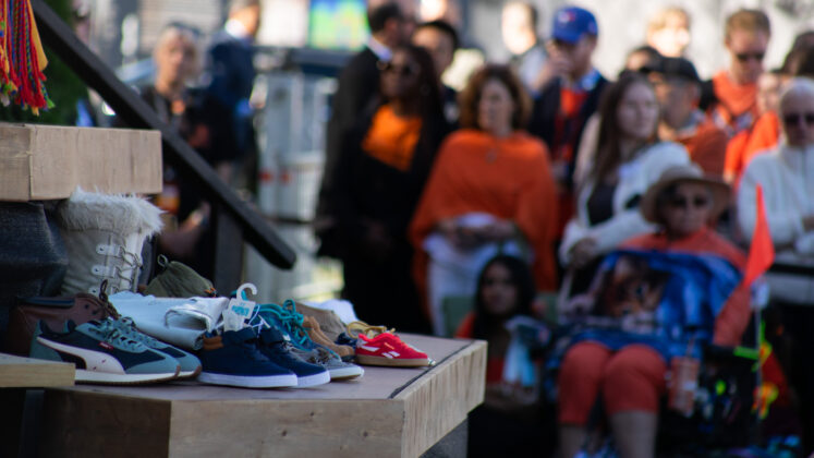 Children's shoes sitting on a platform. Crowd behind wearing orange.