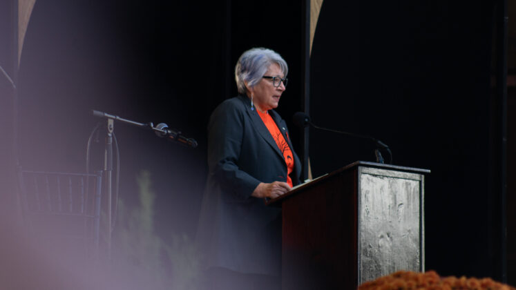 Mary Simon stands at a podium wearing orange