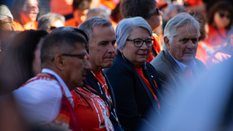 Mark Carney and Mary Simon sit at the front of a crowd wearing orange