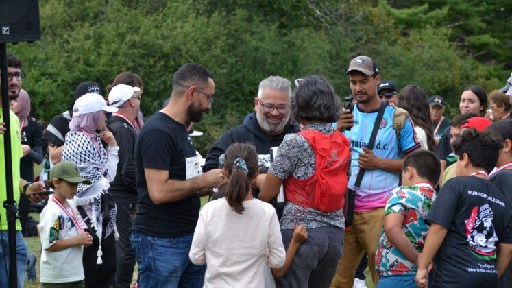 Man gives medal to person surrounded by family in a field.
