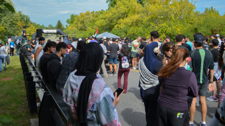 A crowd of people gather around a race starting line.