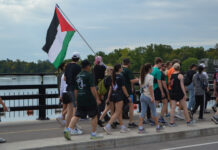 In photos: Hundreds run for Palestinian resistance in Ottawa A group of people wearing athletic clothes walk on a bridge, with one person holding a Palestinian flag