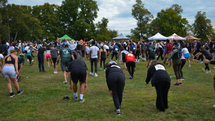 A crowd of people bend down as they stretch in a field with event tents.