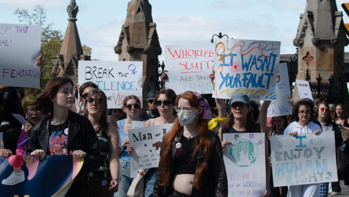 A crowd of people hold several signs as they march on the street. One sign says 