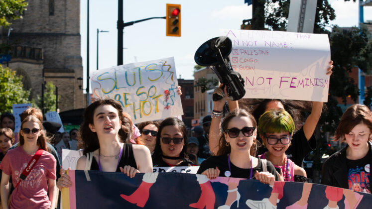 A crowd walks holding posters. One poster says "sluts be so hot."