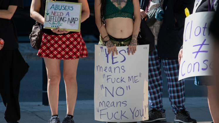 A crowd of people of their necks down with one sign saying "Yes means fuck me, no means fuck you"