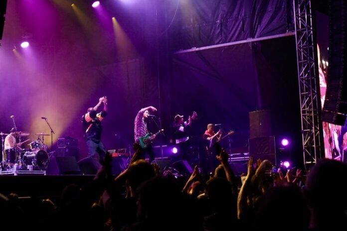 A band performs on stage under purple lighting.