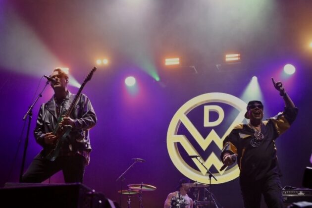 A band performs on stage under purple lighting.