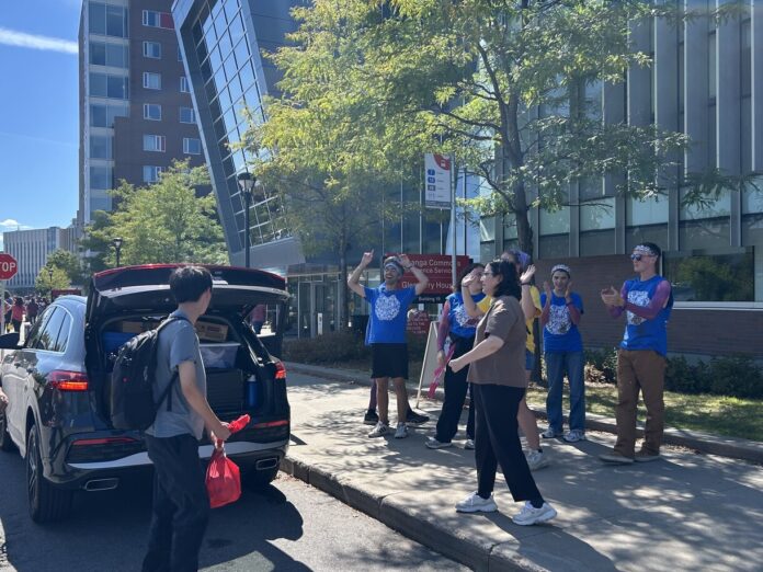 People in blue shirts cheer on person opening up black trunk.