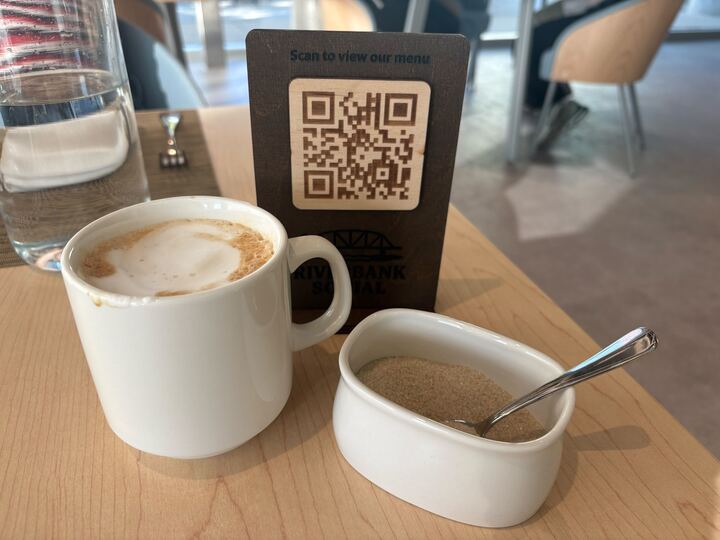 A latte sits on a table next to a bowl of brown sugar.
