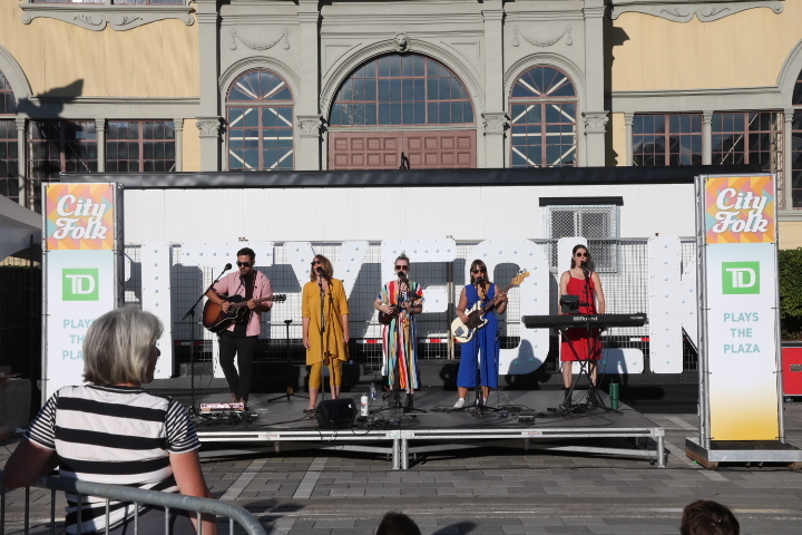 A band performs on a small stage in daylight.