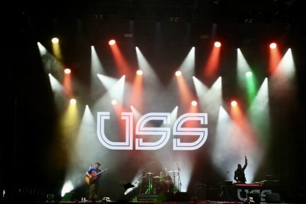 A band performs on stage under multi-coloured lighting.