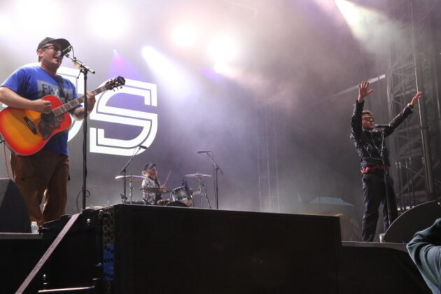 A band performs on stage under multi-coloured lighting.