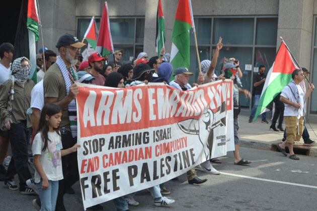 A group of people hold a banner saying "arms embargo now!"