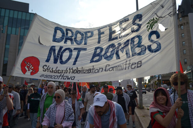 a group of people carry a large banner that says "drop fees, not bombs"