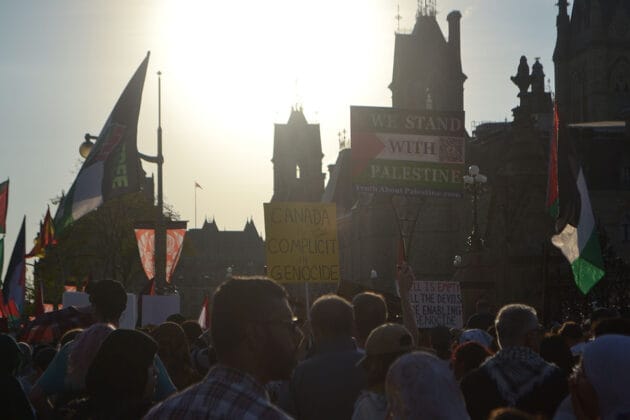 the sun shines on a crowd at parliament hill, with some people holding signs