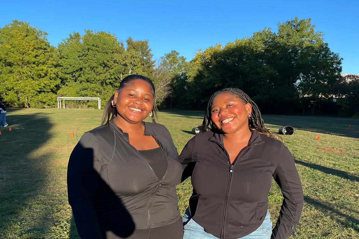 two women stand next to each other in a field
