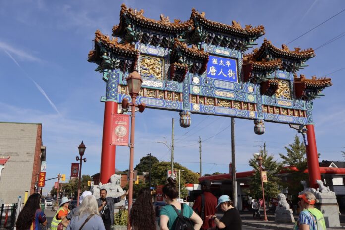 A red arch stands tall against a clear blue sky while a tour guide gives a tour